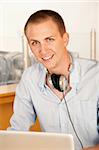 A young man using a laptop. He has headphones draped around his neck. Vertical shot.