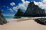 Sandy beach surrounded by rocks taken against deep blue skies covered with few clouds. Picture is taken on Fernando de Noronha Island, Brazil.