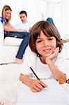 Smiling little boy drawing lying on floor in the living room