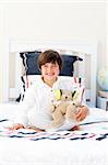 Smiling little boy playing with a teddy bear in his bedroom