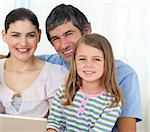 Little girl using a laptop with her parents on the sofa