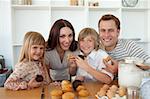 Cute children eating muffins with their parents in the kitchen