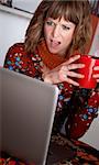 Astonished woman in front of a laptop with drink