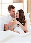 Intimate couple drinking champagne lying in bed at home