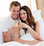 Loving couple drinking champagne lying in bed at home