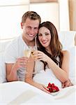 Enamoured couple drinking champagne with strawberries lying in bed at home