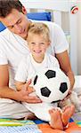 Close-up of a little boy and his father playing with a soccer ball sitting on bed