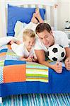 Handsome father and his son playing with a soccer ball lying on bed