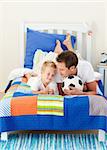 Attractive father and his son playing with a soccer ball lying on bed