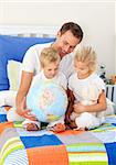 Blond siblings and their father looking at a terrestrial globe sitting on bed