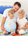 Adorable children and their father looking at a terrestrial globe sitting on bed