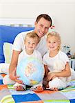 Cute children and their father looking at a terrestrial globe sitting on bed
