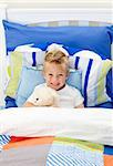 Cute little boy lying in bed with a teddy bear