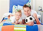 Cute little boy and his father watching a football match in the kid's bedroom