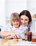 Cute little girl and her mother preparing toasts in the kitchen
