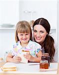 Cute little girl and her mother eating slices of bread in the kitchen