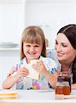 Happy little girl and her mother eating slices of bread in the kitchen