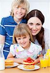 Jolly mother and her children eating waffles with strawberries in the kitchen