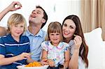 Young family eating crisps while watching TV on the sofa