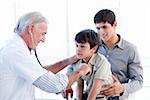 Senior doctor examining a little boy with his father at the practice