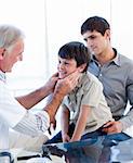 Senior doctor examing little boy throat with his father in the pratice