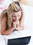 Concentrated woman using a laptop lying on her bed at home