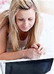 Serious woman using a laptop lying on a bed at home