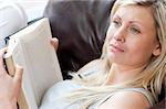 Beautiful woman reading a book sitting on a sofa in a living-room