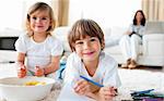 Smiling siblings eating chips and drawing lying on the floor