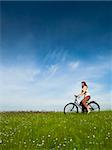 Happy young woman on a green meadow riding a bicycle