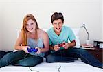 A couple of teenagers playing video games in a bedroom