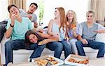 Six teenagers eating pizza in the living-room on the sofa