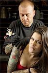 A tattoo artist applying his craft onto the back and arm of a female in her 20's. Focus on female's face.