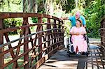 Senior man pushes his disabled wife's wheelchair through the park.