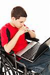 Teen boy in a wheelchair communicating via his laptop computer.  Isolated on white.