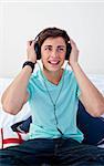 A teenage guy sitting on his bed listening to the music with headphones