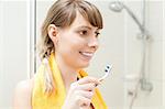 young woman in bathroom brushing teeth and smiling