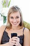 Cheerful woman sending a text sitting on a sofa at home