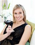 Beautiful blond woman drining red wine sitting on a sofa