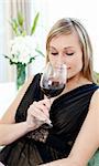 Charming blond woman drining red wine sitting on a sofa