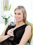 Happy blond woman drining red wine sitting on a sofa