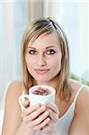 Portrait of a young woman drinking a coffee sitting on a sofa at home