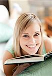 Radiant woman lying on a sofa reading a book at home