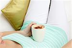 Close-up of a woman drinking a coffee lying on a sofa