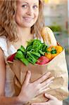 Smiling woman holding a grocery bag in the kitchen