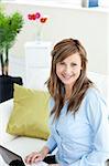 Delighted businesswoman using a laptop sitting on a sofa in a living room