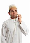 An arab italian mixed race businessman on the telephone.  He is wearing a traditional white middle eastern robe eg Kurta or dishdasha and a white hat called a topi.  White background.