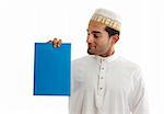 An ethnic mixed race man wearing traditional arab clothing, is holding a brochure, sign, document in hone hand and looking at it.  White background.