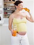 italian 6 months pregnant woman standing near refrigerator and drinking orange juice. Three quarter length, vertical shape