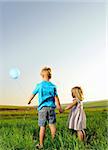 Brother and sister hold hands and hold onto their only balloon